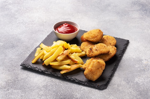 Patatas fritas y nuggets de pollo con salsa de tomate ketchup. Concepto de comida rápida de alimentos poco saludables. Mesa de hormigón gris Copia espacio.