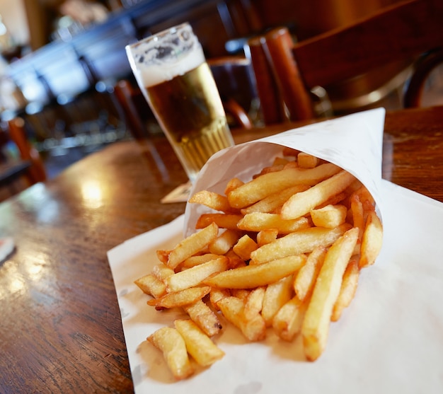 Patatas fritas en una pequeña bolsa de papel blanco sobre una mesa de madera en un pub de Bruselas