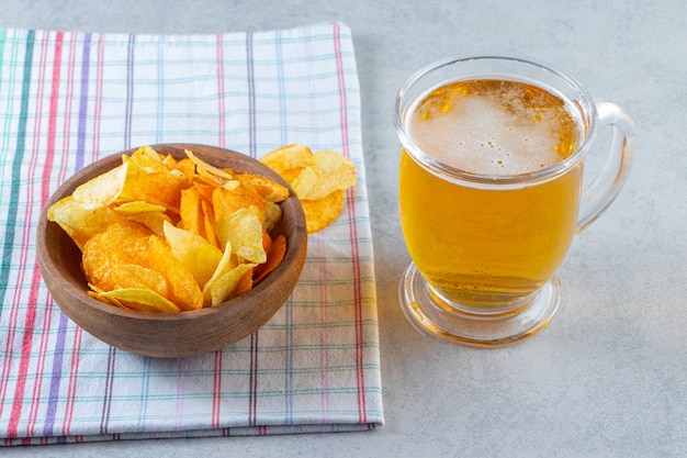 Patatas fritas en un recipiente junto a un vaso de cerveza sobre un paño de cocina, sobre la superficie de mármol.