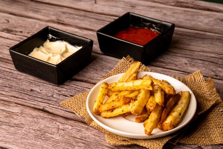 patatas fritas rústicas servidas con salsas mayonesa ketchup sobre un fondo de madera