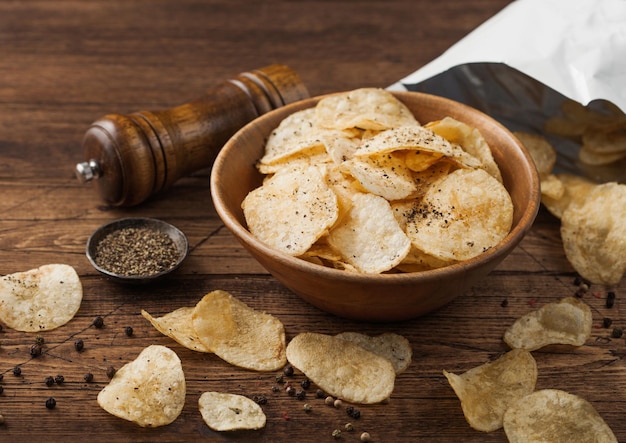 Patatas fritas con sabor a pimienta negra en un cubo de madera sobre fondo de mesa de madera con molino y pimienta molida con paquete