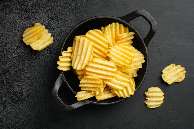 Patatas fritas con sabor a rancho ondulado sobre fondo de mesa de piedra oscura negra vista superior plana