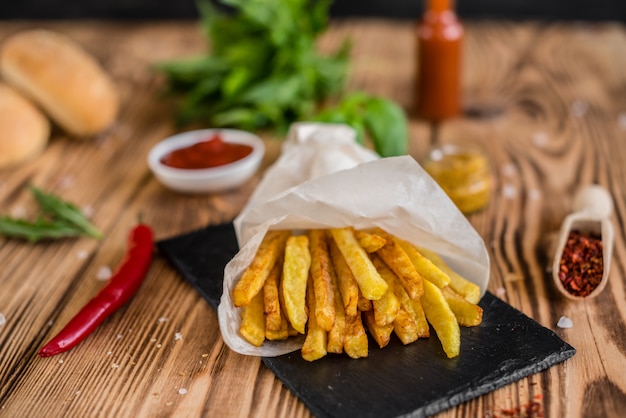 Patatas fritas sabrosas con las verduras contra un fondo oscuro. Comida rápida. Se puede utilizar como fondo.