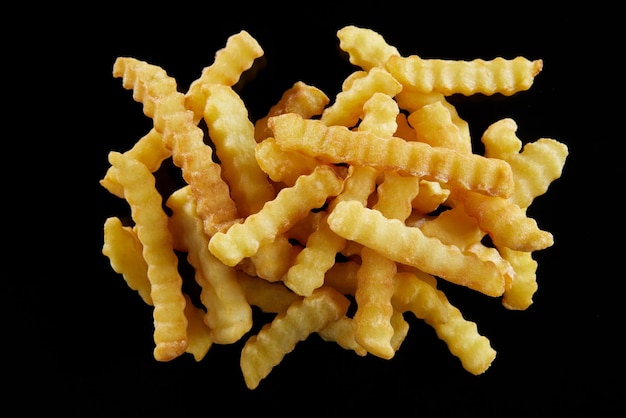 Patatas fritas saladas y crujientes con sal y pimienta roja en una mesa negra.