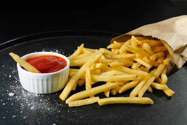 Patatas fritas saladas y salsa de tomate en un primer plano de fondo oscuro Comida rápida