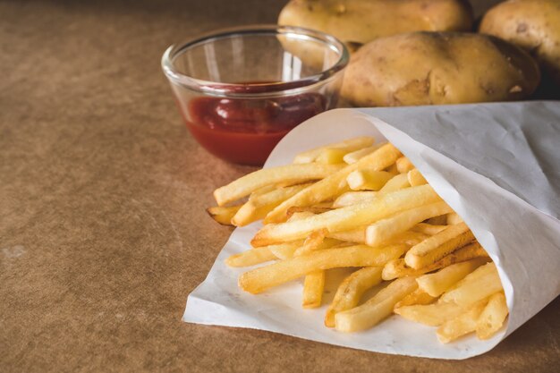 Patatas fritas con salsa de tomate y patatas crudas en la mesa de madera.