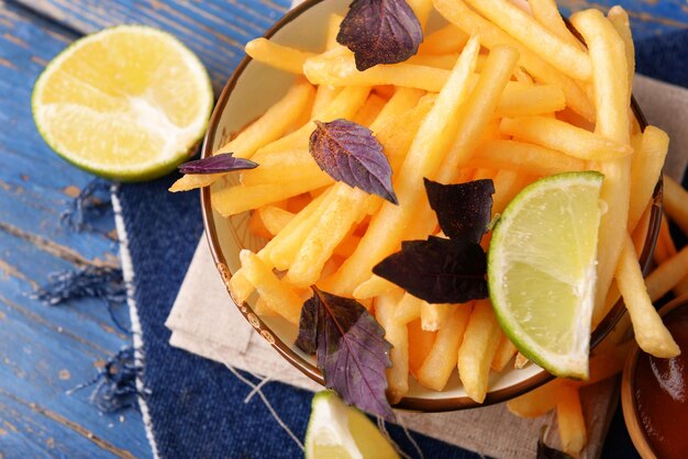 Patatas fritas en un tazón con albahaca y salsa sobre fondo de madera vieja