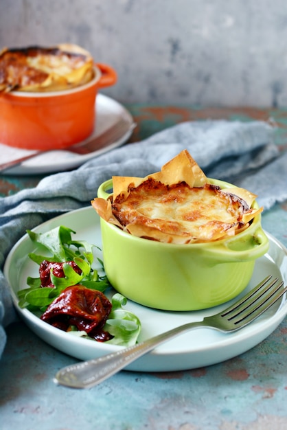 Patatas gratinadas al horno en masa filo, con corteza de queso crujiente y con una ensalada de rúcula, tomates secados al sol y queso sobre una pared azul. Un plato de cocina francesa.