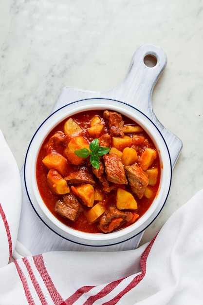 Patatas guisadas con carne en salsa de tomate con especias y hierbas sin gente en una mesa blanca