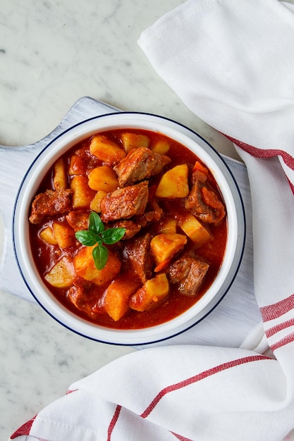 Patatas guisadas con carne en salsa de tomate con especias y hierbas sin gente en una mesa blanca