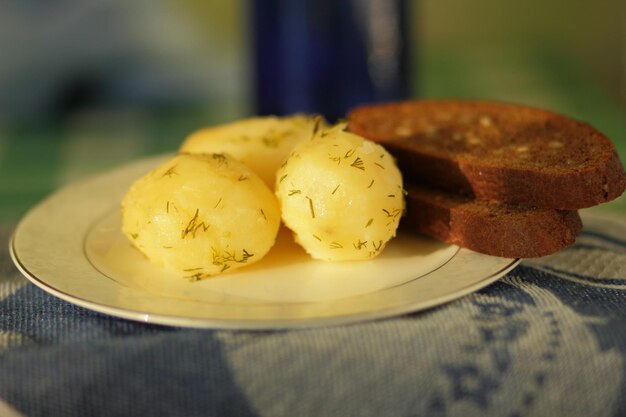 Patatas hervidas con eneldo y pan negro en un plato blanco con una servilleta azul Primer plano de una sabrosa comida saludable en la cocina casera Concepto de comida vegetariana