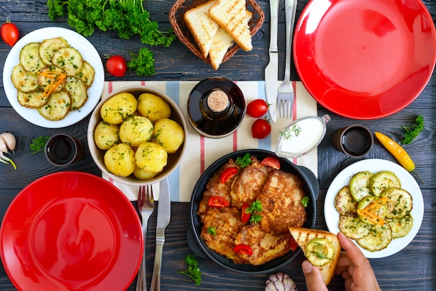 Patatas hervidas, rodajas de calabacín frito, escalopes en una mesa de madera. Vista superior. Mesa servida para la cena familiar, almuerzo. Estilo rústico