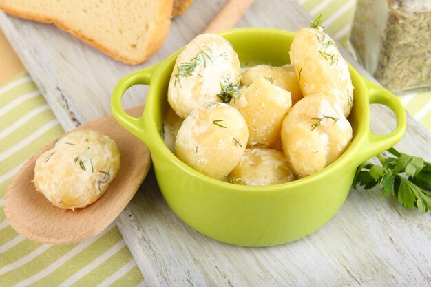 Patatas jóvenes tiernas con crema agria y hierbas en una sartén sobre una tabla de madera en el primer plano de la mesa