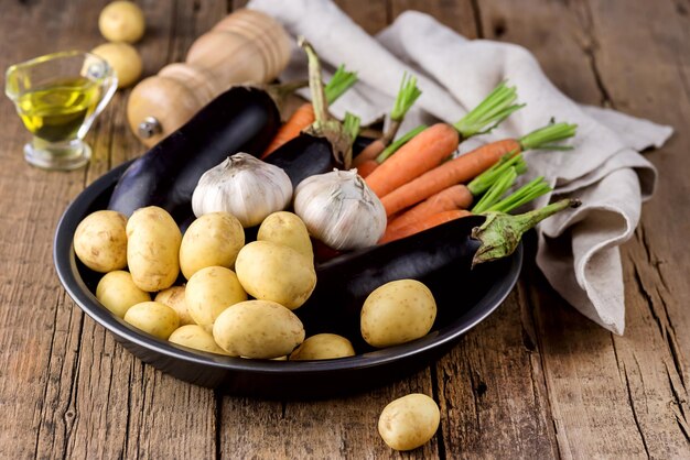 Patatas jóvenes Zanahoria Ajo y berenjena en plato negro Variedad de verduras crudas listas para cocinar