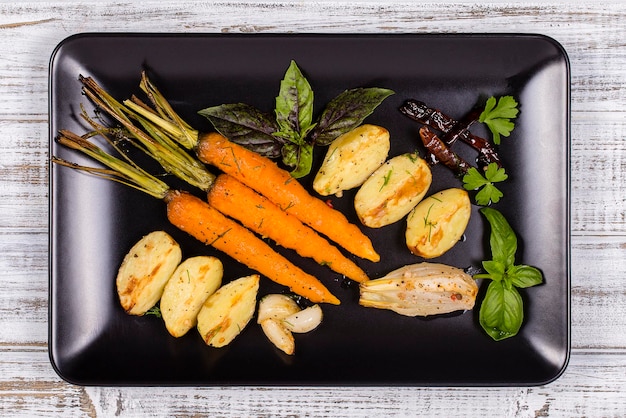 Patatas jóvenes zanahorias cebollas pimientos ajo horneado en el horno en el plato negro vista superior de cerca