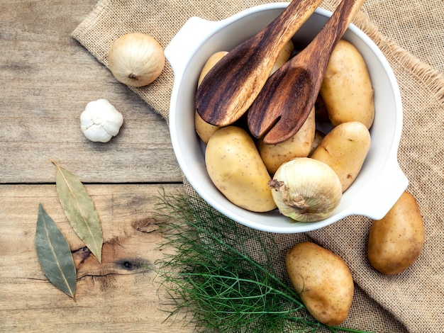 Patatas orgánicas frescas en bolsa de cáñamo de cáñamo con los ingredientes en la mesa de madera rústica.