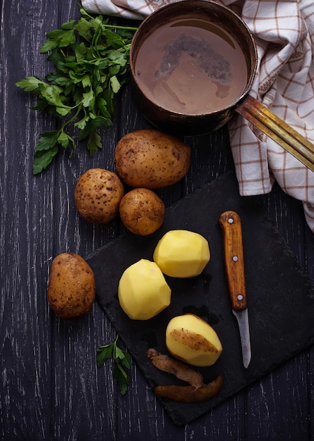 Patatas peladas sin cocer sobre fondo oscuro