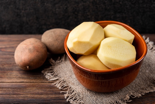 Patatas peladas crudas en un recipiente sobre la superficie de madera oscura.