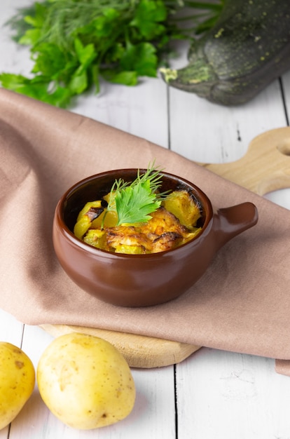 Patatas, pollo y calabacín al horno en una cazuela de barro sobre un fondo claro.