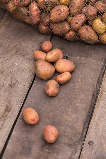 Patatas recién cosechadas con tierra todavía en la piel, derramándose de una bolsa de arpillera, sobre una paleta de madera rugosa.