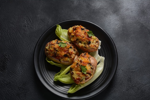 Patatas rellenas al horno con tocino, cebolla verde, champiñones y queso en un plato negro