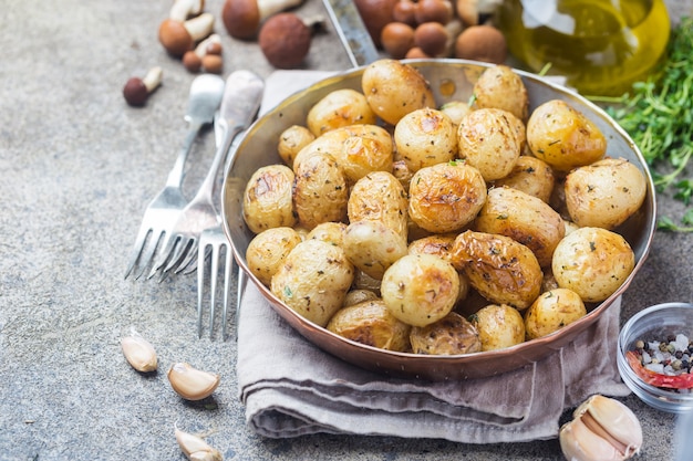 Patatas tiernas asadas con verduras y aceite de ajo en una sartén sobre piedra gris