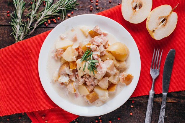 Patatas con tocino y pera en la mesa, plato de restaurante en una vista superior de fondo de madera