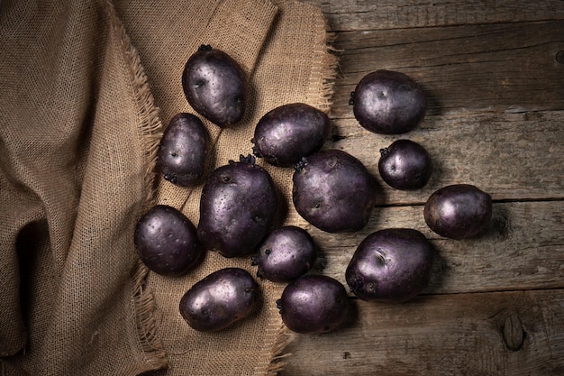 Patatas vitelotte violetas crudas sobre tablas de madera y tela de arpillera Patatas moradas sobre tela de saco de lino Vista superior