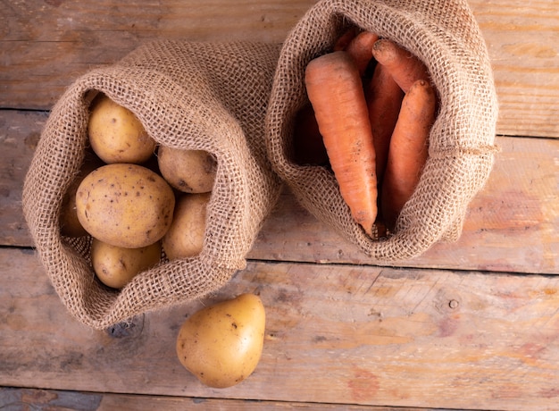 Patatas y zanahorias en una tela de saco en una mesa de madera. concepto ecológico