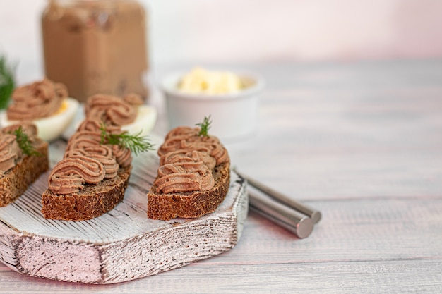 Paté de hígado de pollo casero con zanahorias, cebolla y mantequilla. Decorado con una ramita de eneldo. Lubricado en pan. En la mesa blanca