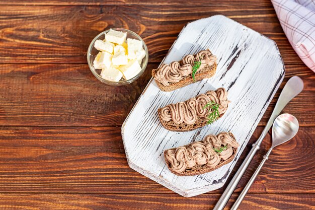 Paté de hígado de pollo casero con zanahorias, cebolla y mantequilla. Decorado con una ramita de eneldo. Lubricado en pan. Sobre una mesa de madera.