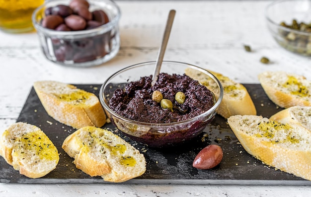 Paté de oliva en un tazón con crostini sobre tabla de cortar de piedra negra