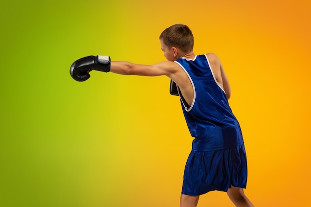 Pateando. Entrenamiento de boxeador profesional adolescente en acción, movimiento aislado sobre fondo degradado en luz de neón. Patear, boxear. Concepto de deporte, movimiento, energía y estilo de vida dinámico y saludable.