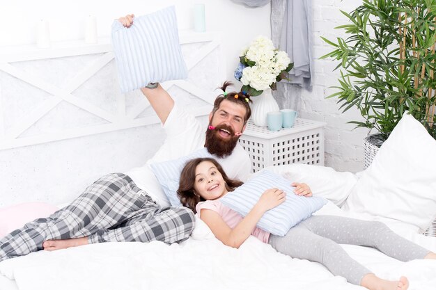 Paternidad feliz Hombre hipster barbudo con peinado infantil colas de caballo coloridas e hija en pijama Chico y chica relajándose en el dormitorio Estilo pijama Divirtiéndose fiesta de pijamas Fiesta de pijamas