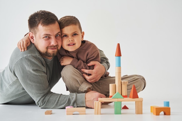 Paternidade Filho e pai brincando com brinquedo de tijolos coloridos em fundo branco Pai cuida de seu filho