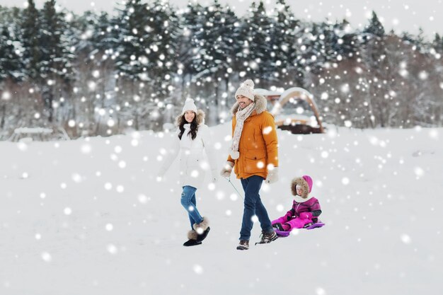 paternidade, moda, temporada e conceito de pessoas - família feliz com criança no trenó andando na floresta de inverno