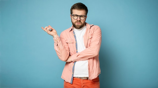 Pathos pompöser junger bärtiger Mann mit Brille zeigt eine Handbewegung zur Seite und blickt in die Kamera