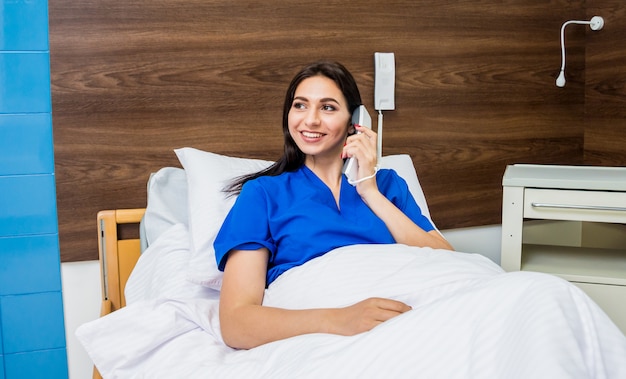 Patient, der im Krankenhausbett am Telefon spricht. Junge kaukasische Frau.