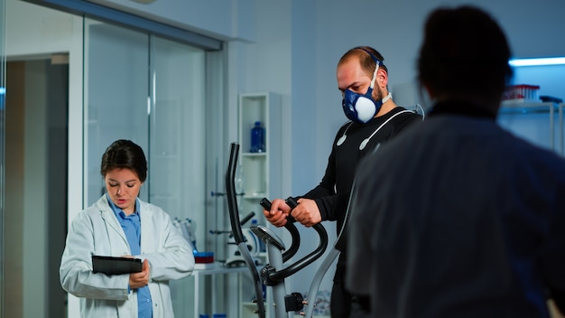 Patient macht Elektrokardiogramm während der körperlichen Betätigung im Sportwissenschaftslabor, überwacht Ausdauer und Herzfrequenz, Computer zeigt EKG-Daten auf dem Display an. Mann läuft mit Maske und medizinischen Elektroden