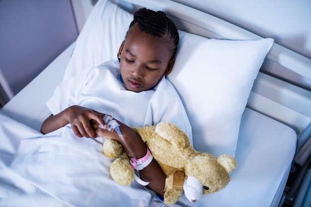 Patient schläft mit Teddybär auf dem Bett im Krankenhaus