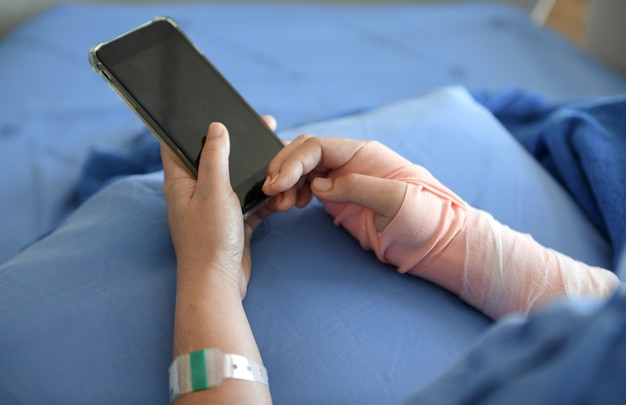 Patient trägt eine Schiene im Arm. Er spielt Smartphone.
