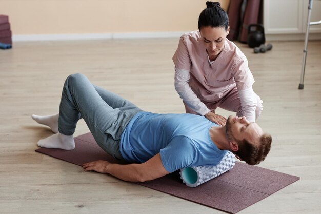 Patient trainiert mit einem Massagegerät zusammen mit einem Therapeuten im Krankenhaus auf einer Trainingsmatte