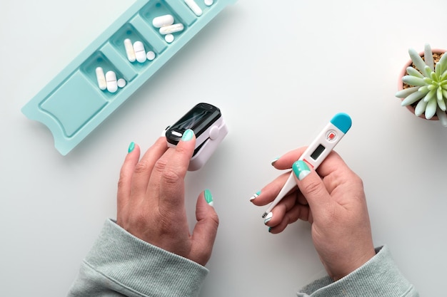 Patientenhände mit Pillen und Pulsoximeter-Finger digitales Gerät zur Messung der Sauerstoffsättigung in der Lunge Reife kaukasische Frauenhände Reduzierte Sauerstoffversorgung ist ein Zeichen für eine Lungenentzündung