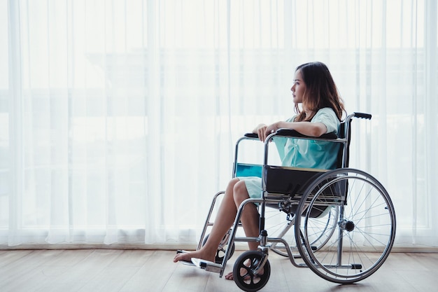 Patientin im grünen Hemd sitzt auf dem Rollstuhl der Krankenhausklinik im Patientenzimmer. Junge Patientin erholt sich wegen Krankheit in einem Krankenzimmer.