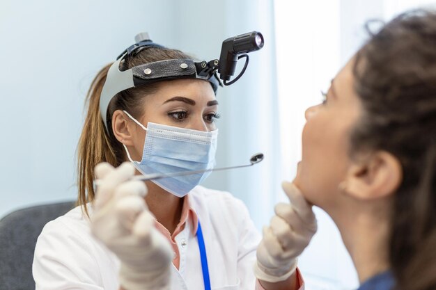 Patientin öffnet den Mund für den Arzt, um in den Hals zu schauen Ärztin untersucht Halsschmerzen des Patienten in der Klinik Hals-Nasen-Ohrenarzt untersucht Halsschmerzen des Patienten