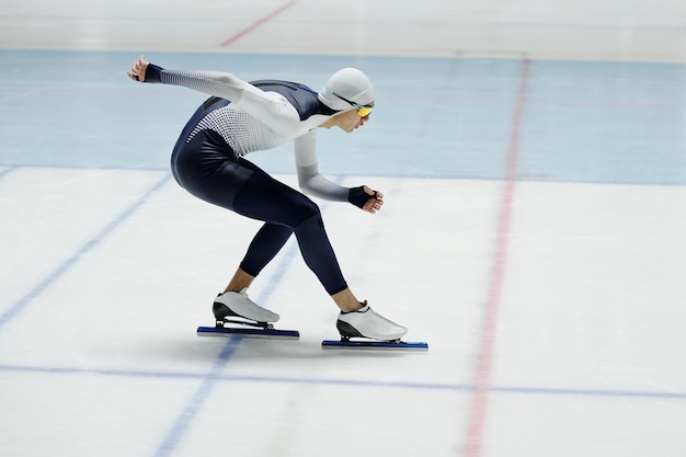Patinador de velocidade curvado para a frente sobre a pista de gelo enquanto se move ao longo da arena