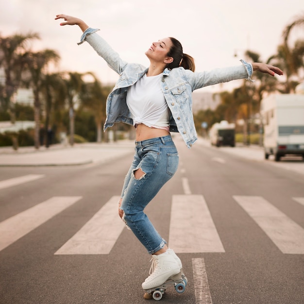 Patinador femenino joven sonriente que balancea en el paso de peatones