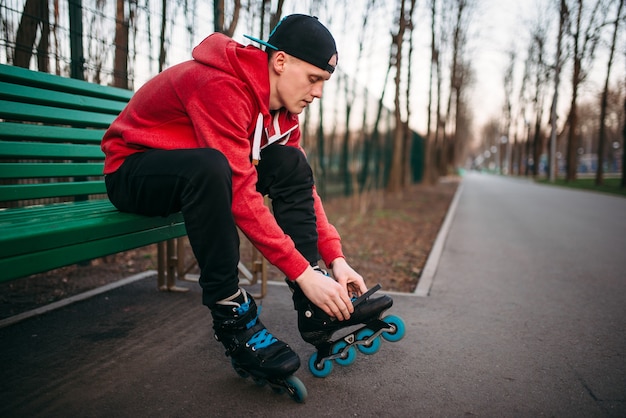 Patinador sentado no banco e amarrando os patins