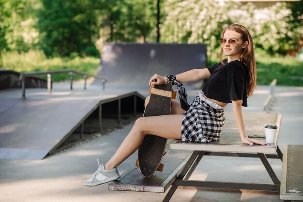 Una patinadora adolescente se está relajando en el banco con una patineta en el parque de patinadores