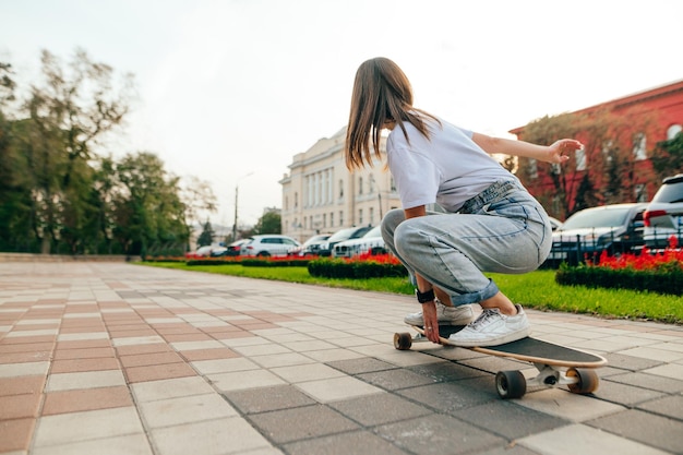 patinadora con ropa informal montando su monopatín en un pavimento de hormigón en un parque de la ciudad